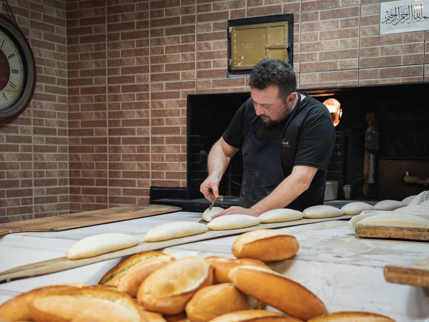 Baker shaping loaves in front of a wood-fired oven
